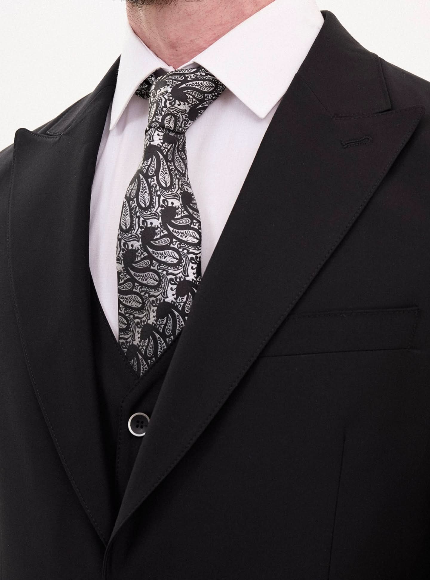 Close-up of a man in a black slim fit suit with a stylish paisley tie, ideal for formal events.