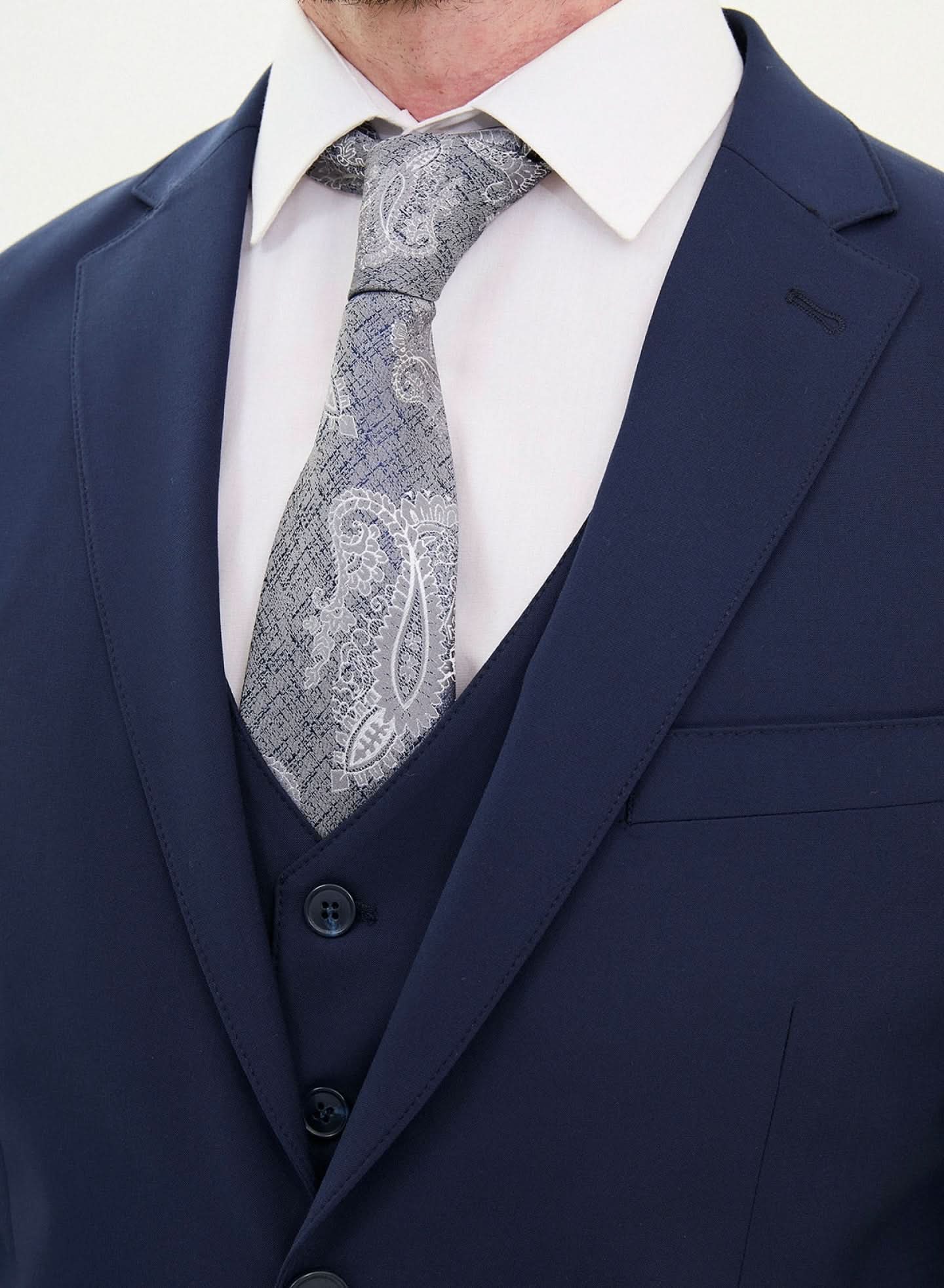 Close-up of a man wearing a dark blue slim fit suit with a paisley tie and white shirt.