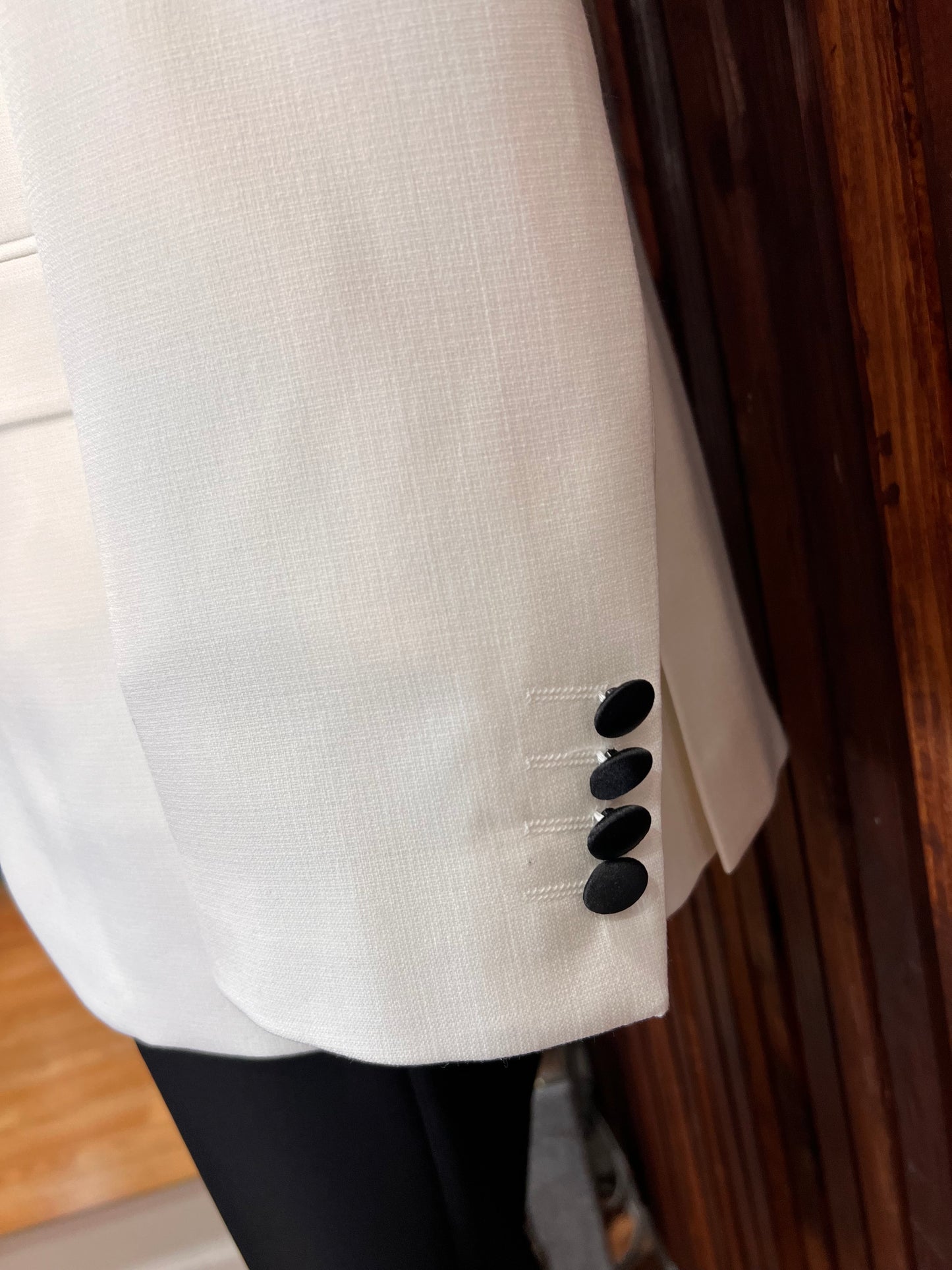 Close-up of men's white tuxedo sleeve showcasing black buttons on a tailored slim fit design.