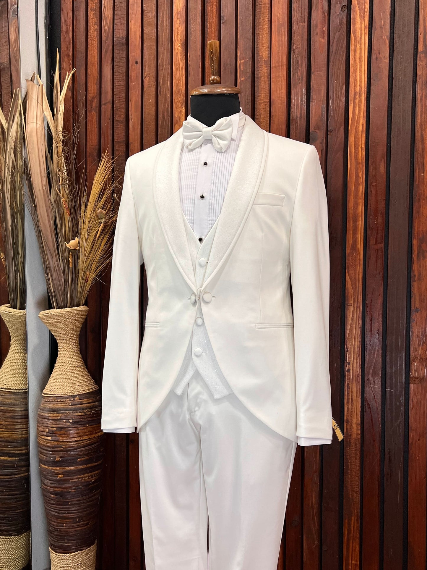 Men’s off-white tuxedo with glittery shawl lapel displayed on a mannequin against a wooden backdrop.