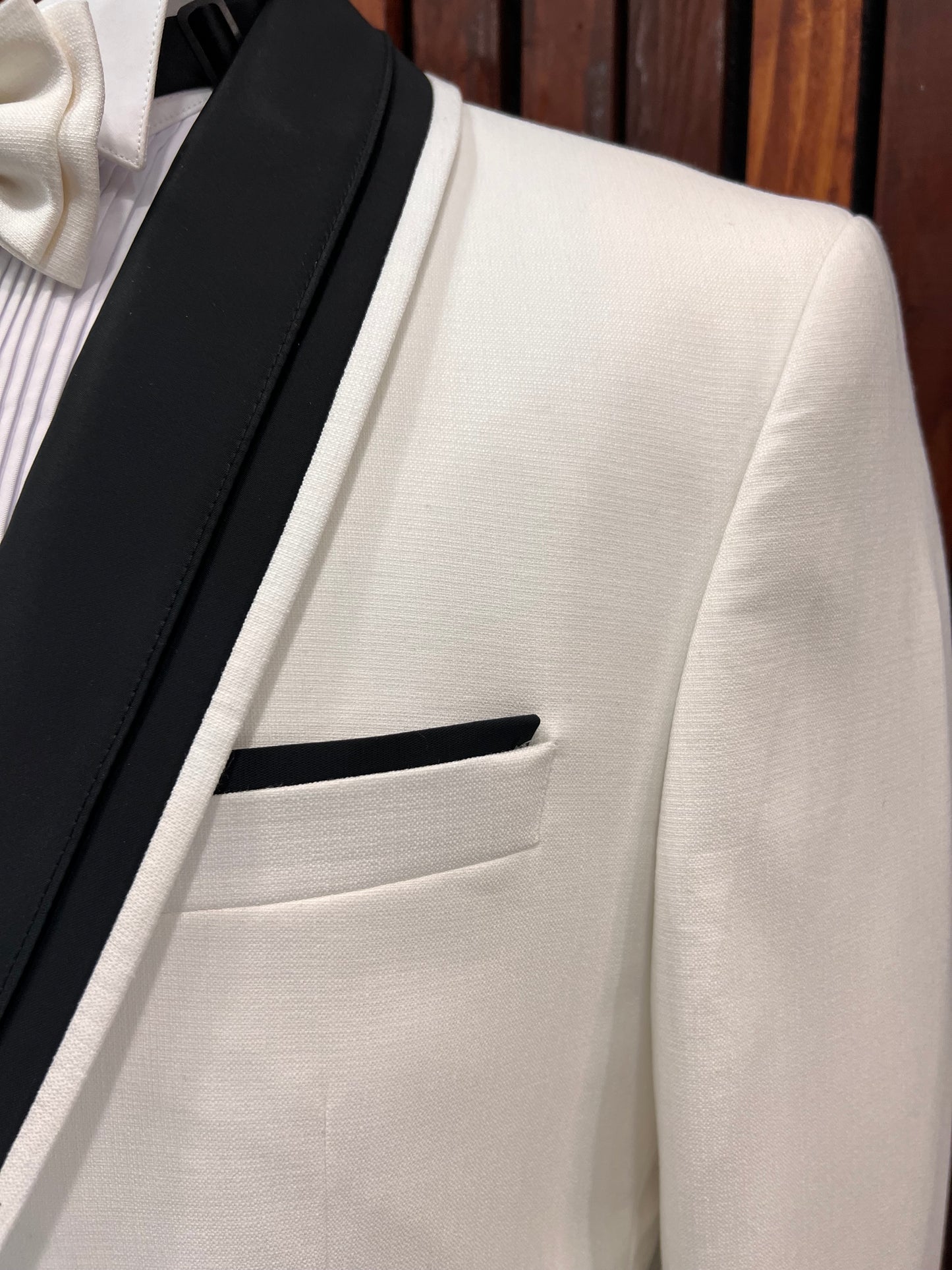 Close-up of men's white tuxedo with black shawl lapel and pocket detail, ideal for formal events.