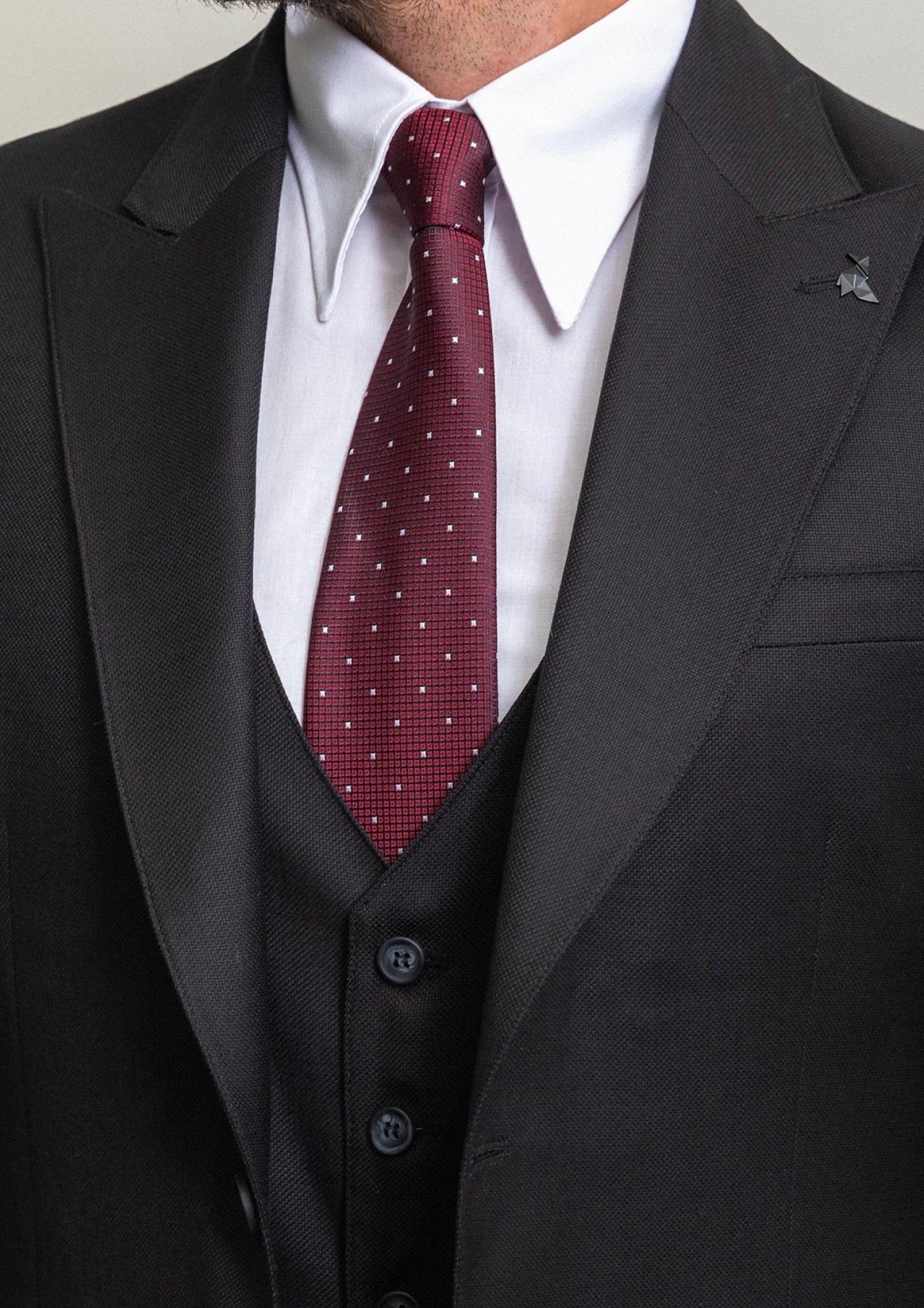 Elegant close-up of a man in a black wool suit with a burgundy polka dot tie, perfect for formal events.