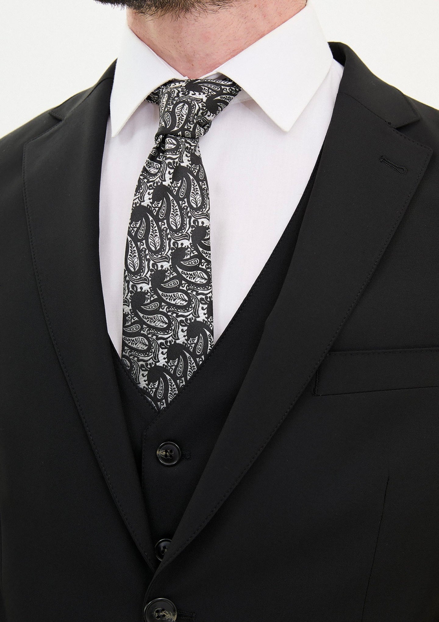 Close-up of a man in a black slim fit suit with a paisley patterned tie, showcasing sophisticated formal wear.