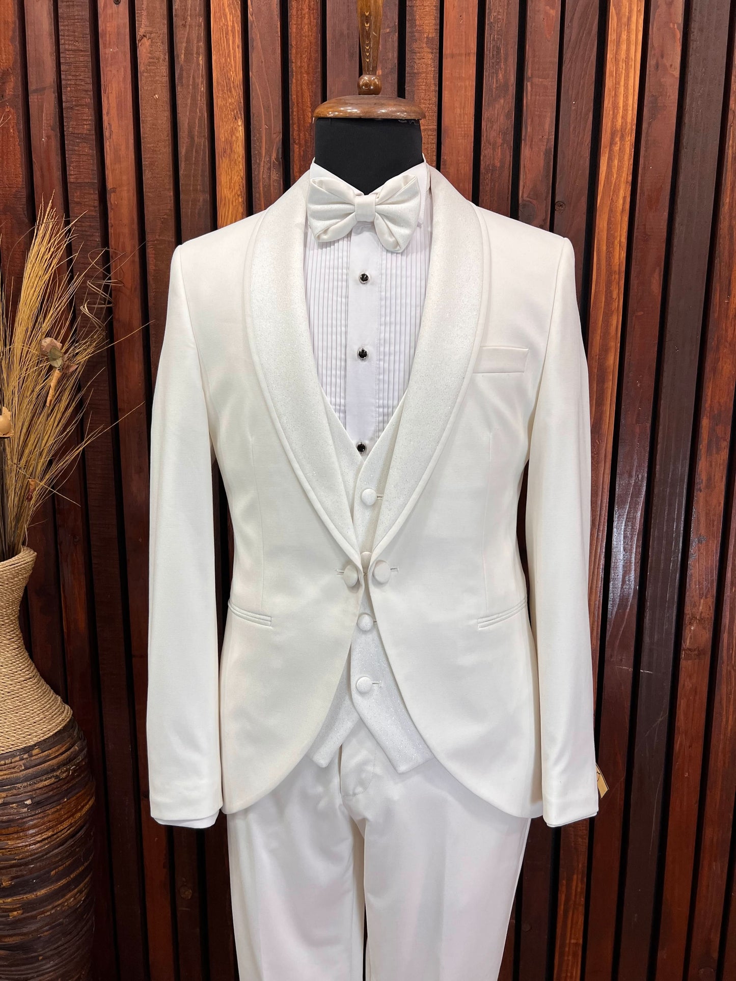 Men's off-white tuxedo with glittery shawl lapel and bow tie on mannequin, ideal for formal events.