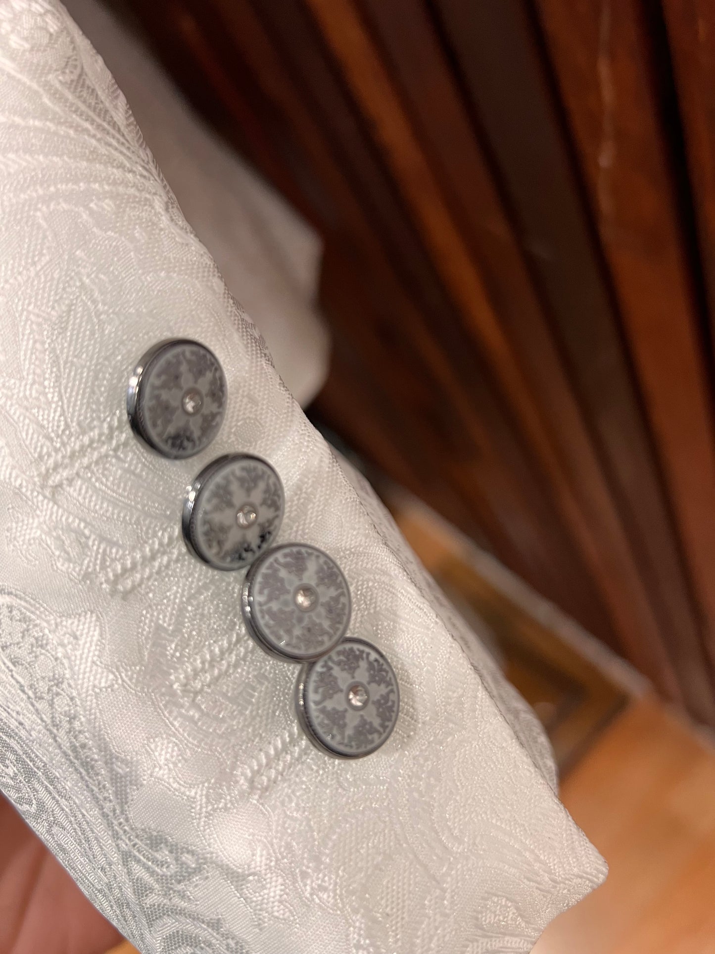 Close-up of elegant buttons on the sleeve of a men's white floral tuxedo with mandarin collar.