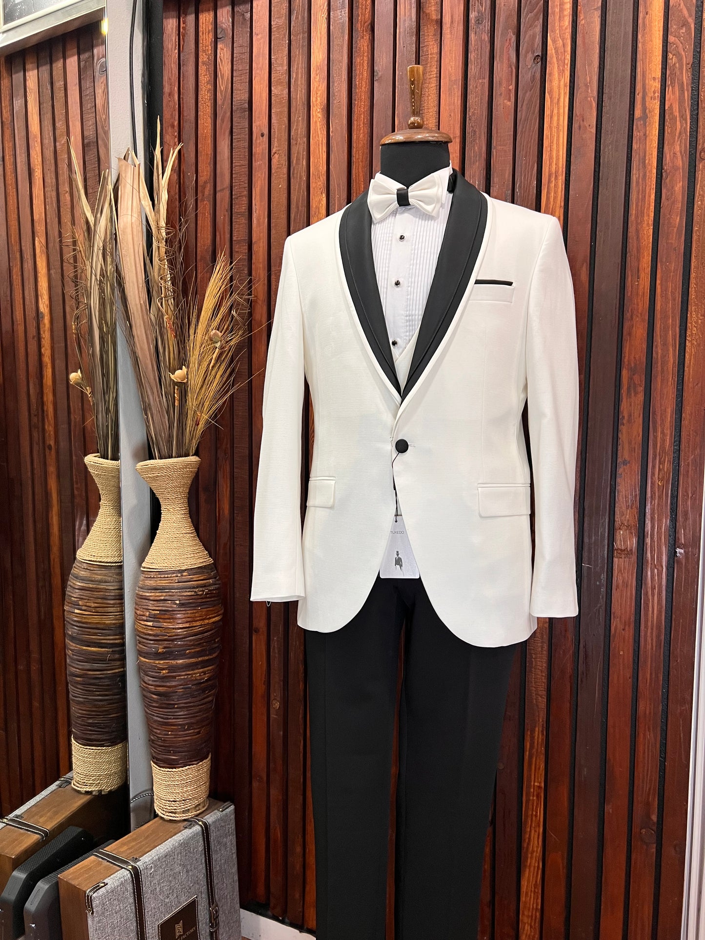 Men’s white tuxedo with black shawl lapel displayed on mannequin in elegant setting.