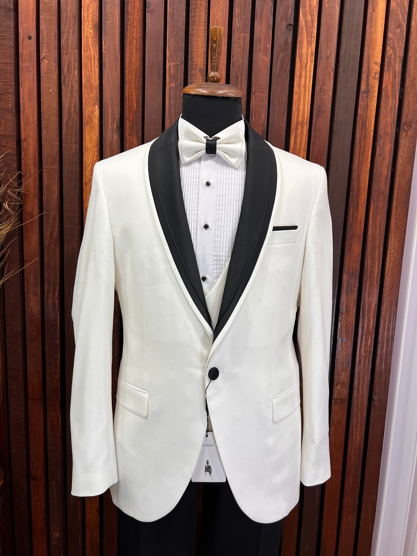 Men's white tuxedo with black shawl lapel and bow tie on display, perfect for formal events and weddings.