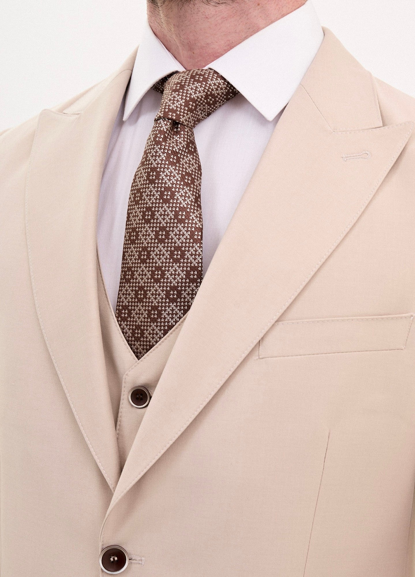 Close-up of a men's stone beige slim fit 3-piece suit with a patterned tie, showcasing stylish formal wear.