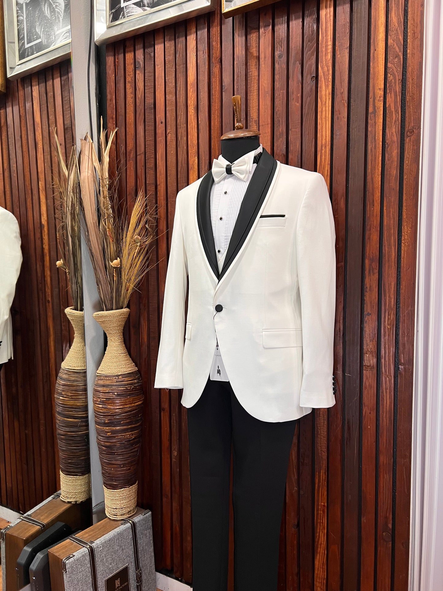 Men's white tuxedo with black shawl lapel displayed on a mannequin against a wooden background.